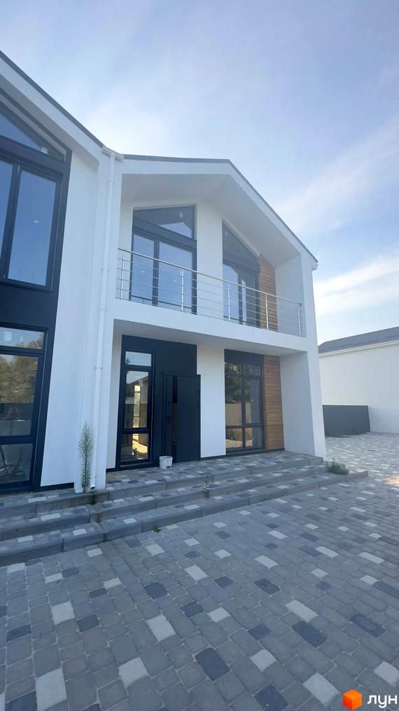 Білий двоповерховий дуплекс Family House з темними вікнами та балконом. Прибудинкова територія вимощена сірою бруківкою.