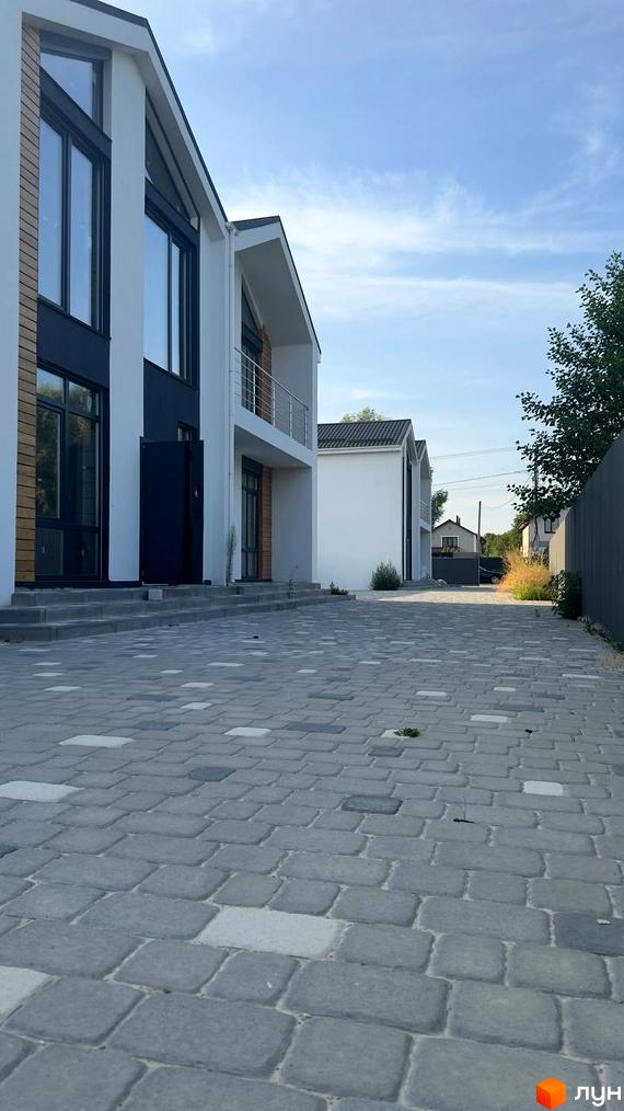 Фасади дуплексів Family House з білими стінами та великими темними вікнами. Перед будинками вимощена бруківкою територія.