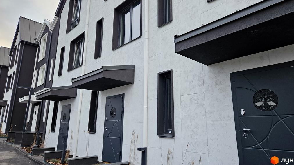 Таунхаус New Smart 15 – фасади будівель з білою та чорною обробкою, великі вікна та сучасні двері. Перед будинками доглянута територія з рослинністю.