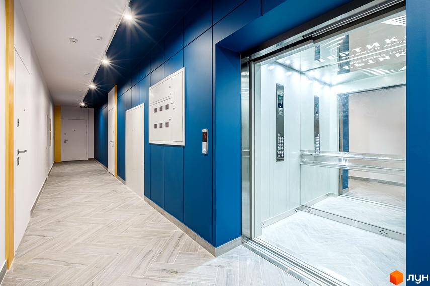 Сучасний коридор житлового комплексу HydroPark DeLuxe з синіми стінами та ліфтом. Підлога оздоблена плиткою з геометричним візерунком.