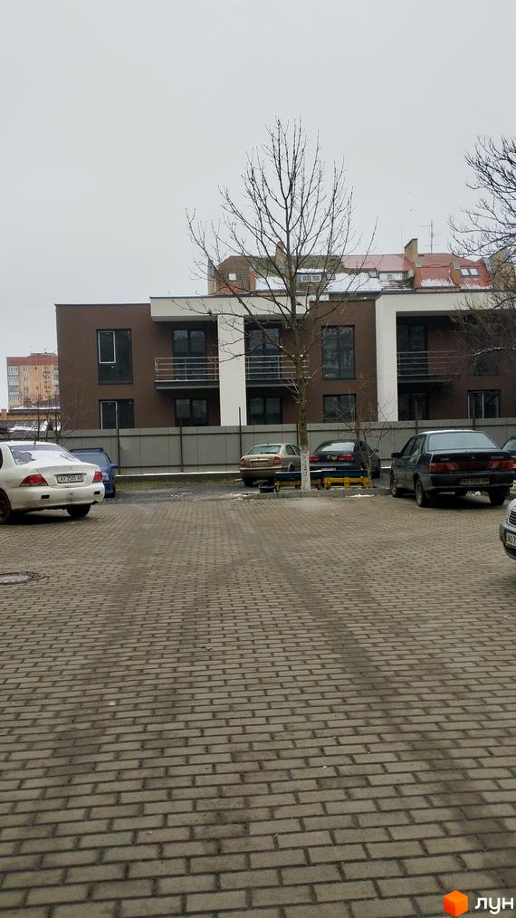 Новобудова на вулиці Володимирська, 65а. Прибудинкова територія з парковкою та деревами.
