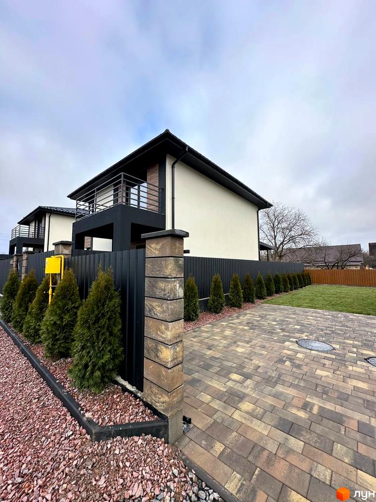 Зовнішній вигляд двоповерхових будинків з балконами та парканом з туй. Прибудинкова територія з бруківки та газону.