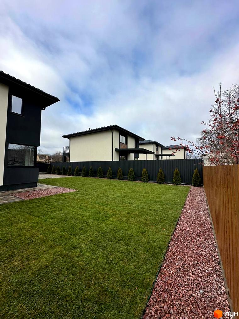 Сучасний житловий комплекс на вул. Яблунська, 20, з акуратною зеленою галявиною та доріжкою з червоної гальки.