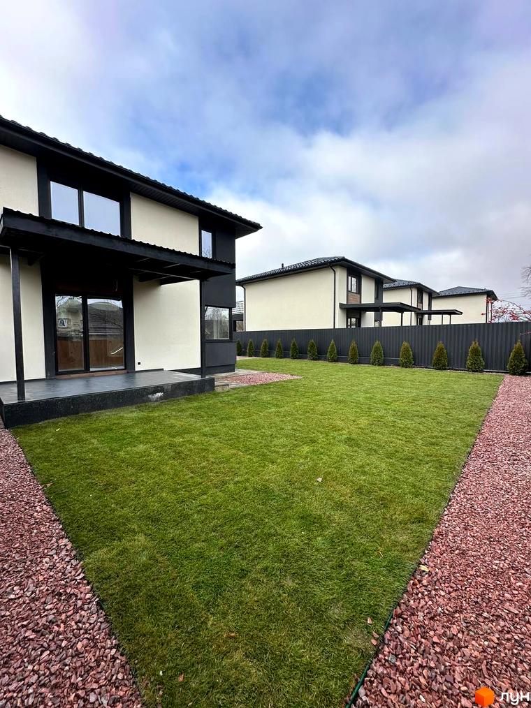 Зовнішній вигляд двоповерхових будинків з темним дахом та фасадом світлого кольору. Прибудинкова територія з доглянутим газоном та гравійними доріжками.