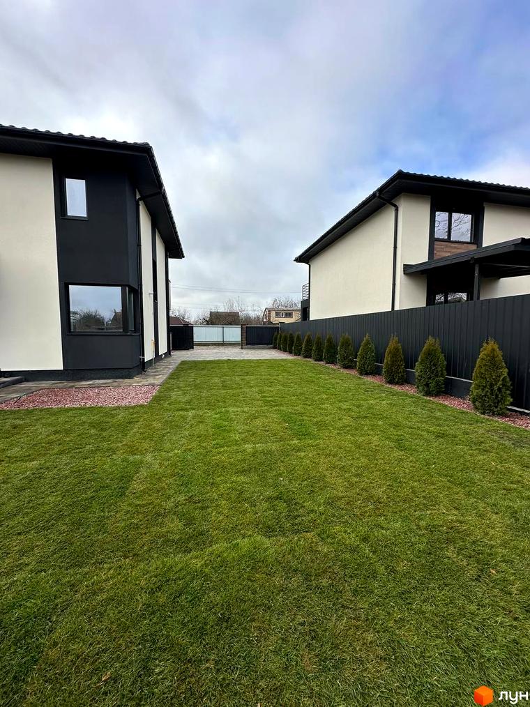 Двоповерховий будинок з чорно-білим фасадом та доглянутою зеленою галявиною перед ним. На задньому плані видно паркан та дерева.