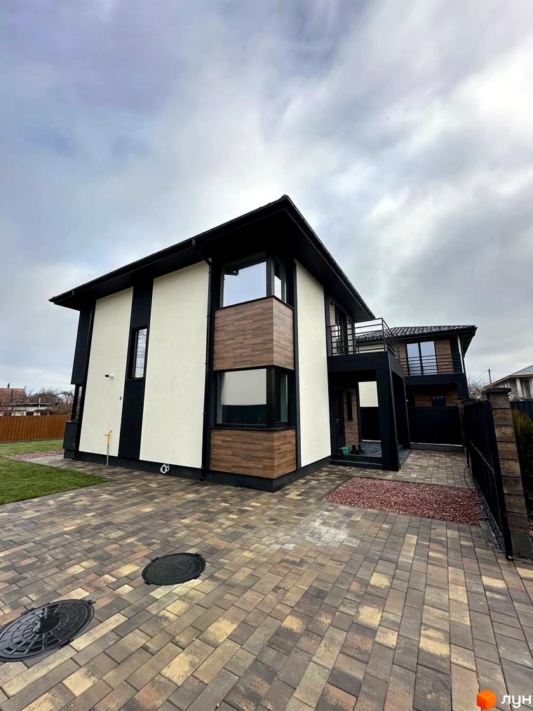 Новобудова на вул. Яблунська, 20 з фасадом з білої та коричневої плитки та чорними елементами. Прибудинкова територія вимощена бруківкою.