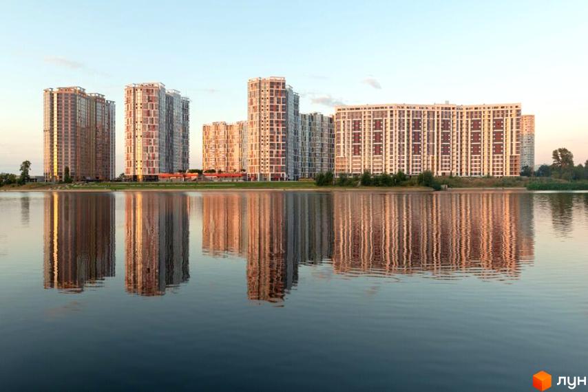 Новобудова Русанівська Гавань: панорама висотних житлових будинків на березі водойми, що яскраво відбиваються у воді.