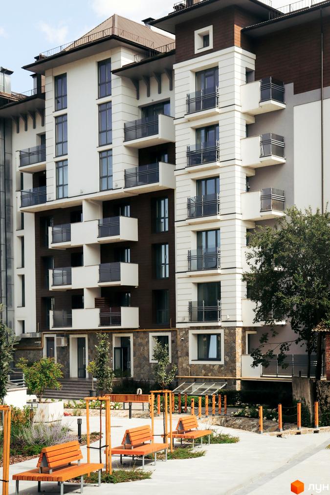 Новобудова Крайобраз з балконами та панорамними вікнами. Прибудинкова територія з лавками та зеленими насадженнями.