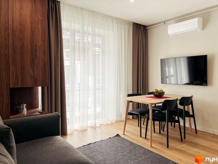 Інтер'єр квартири в ЖК Крайобраз: обідня зона з дерев'яним столом та чорними стільцями, телевізор на стіні та кондиціонер. Простора вітальня з диваном та шторами.