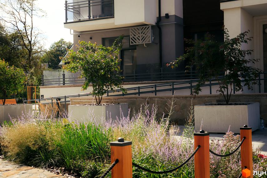 Житловий комплекс Крайобраз: фасад будівлі з балконами та прибудинкова територія з зеленими насадженнями та квітковими клумбами.