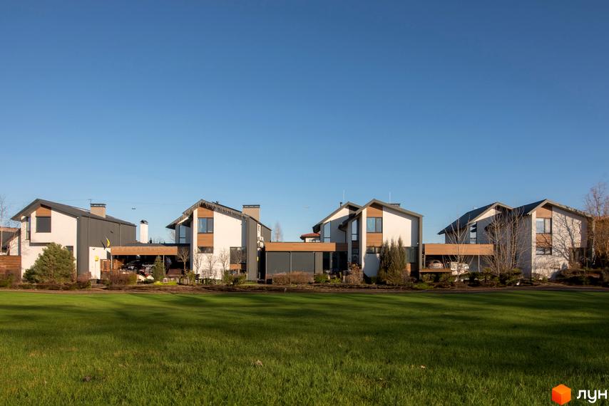 Котеджне містечко КМ Balaton Village. Сучасні будинки з дерев'яними елементами та великими вікнами на тлі блакитного неба. Доглянута зелена галявина перед будинками.