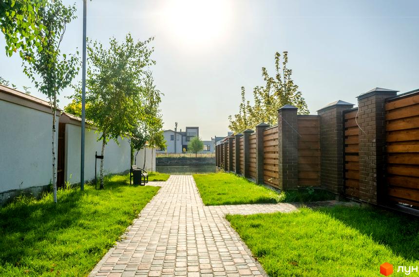 Котеджне містечко Balaton Village: доглянута прибудинкова територія з брукованою доріжкою та зеленими газонами. Сучасні будинки на фоні ясного неба.