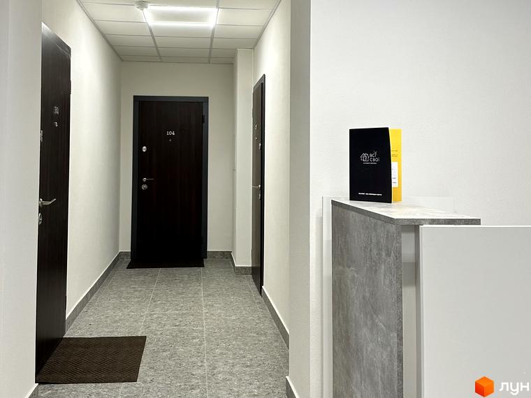 Житловий комплекс Всі Свої. Коридор з дверима та килимами. Брошура з логотипом проєкту на стійці.