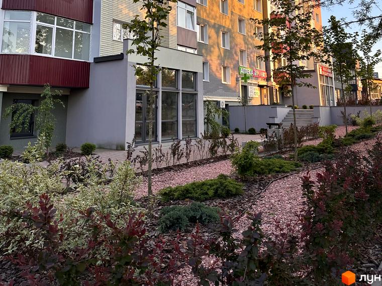 Житловий комплекс Всі Свої. Фасад будинку з вікнами та балконами, прибудинкова територія з ландшафтним дизайном та рослинами.