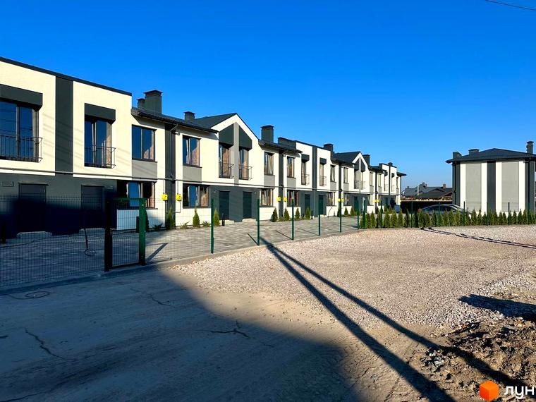 Таунхауси COMFORT RESIDENCE - це двоповерхові будинки з балконами та темними вікнами, розташовані на території з бруківкою та зеленими насадженнями.