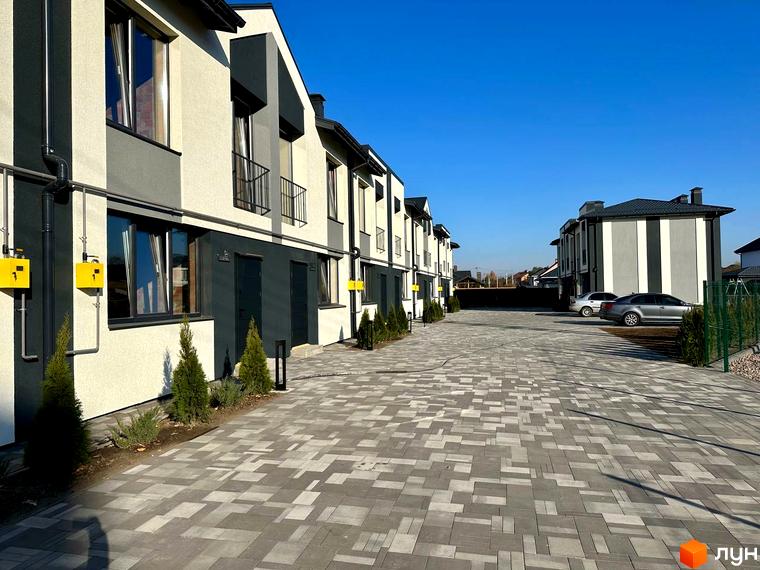 Зовнішній вигляд таунхаусів COMFORT RESIDENCE з фасадами в світлих тонах та темними елементами. Бруківка на прибудинковій території.