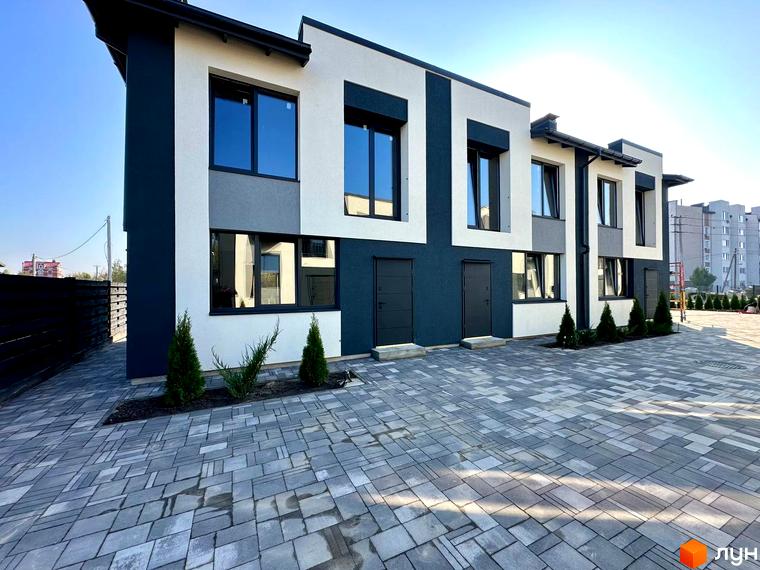 Таунхауси COMFORT RESIDENCE з сіро-білим фасадом та великими вікнами, розташовані на вимощеній сірою плиткою прибудинковій території з молодими туями.