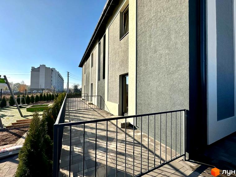 Таунхауси COMFORT RESIDENCE з сірим фасадом та дерев'яною терасою. Поруч зелені насадження та дитячий майданчик.