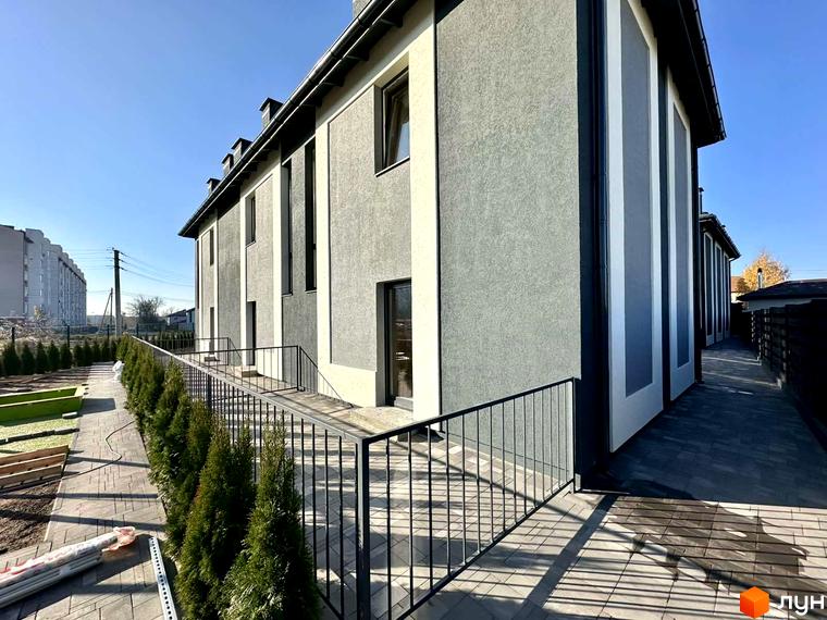 Таунхауси COMFORT RESIDENCE з сірою та білою фасадною обробкою та акуратною прибудинковою територією з туями та бруківкою.