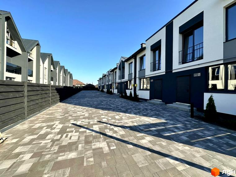 Таунхауси COMFORT RESIDENCE з біло-темними фасадами та брукованою прибудинковою територією під блакитним небом.