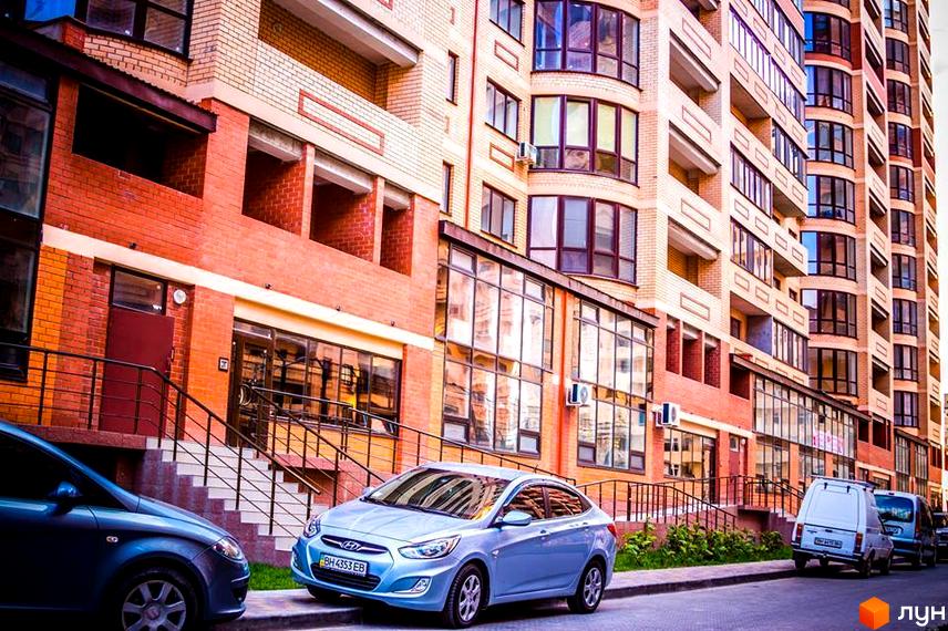 Багатоповерховий будинок Житлового комплексу Армійський з цегляним фасадом та великими вікнами. Перед будинком припарковані автомобілі та є зелені насадження.