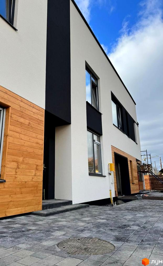 Котеджне містечко КМ Central Town: фасади будівель з дерев'яними елементами та сіра бруківка на прибудинковій території.