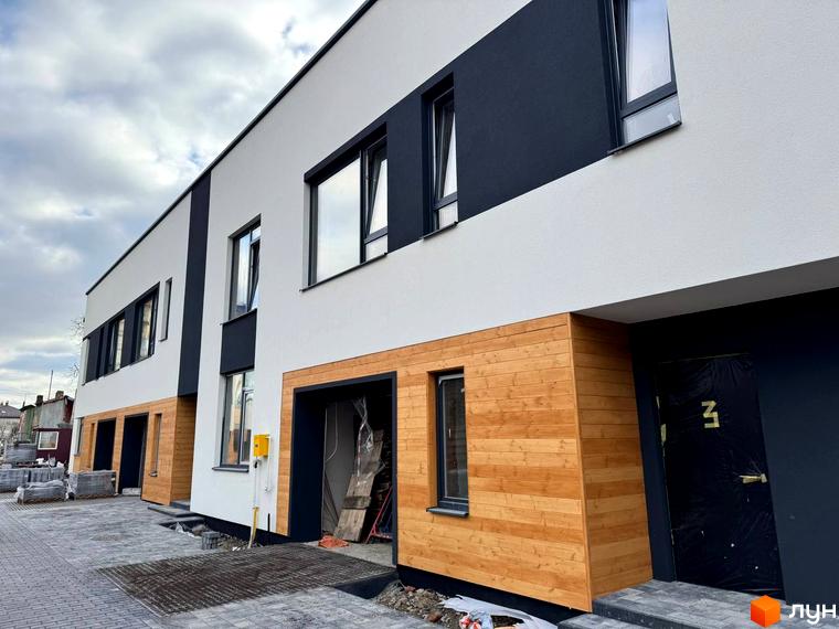 Котеджне містечко КМ Central Town: фасади будинків з дерев'яним оздобленням та великими вікнами. Прибудинкова територія з бруківкою та будівельними матеріалами.