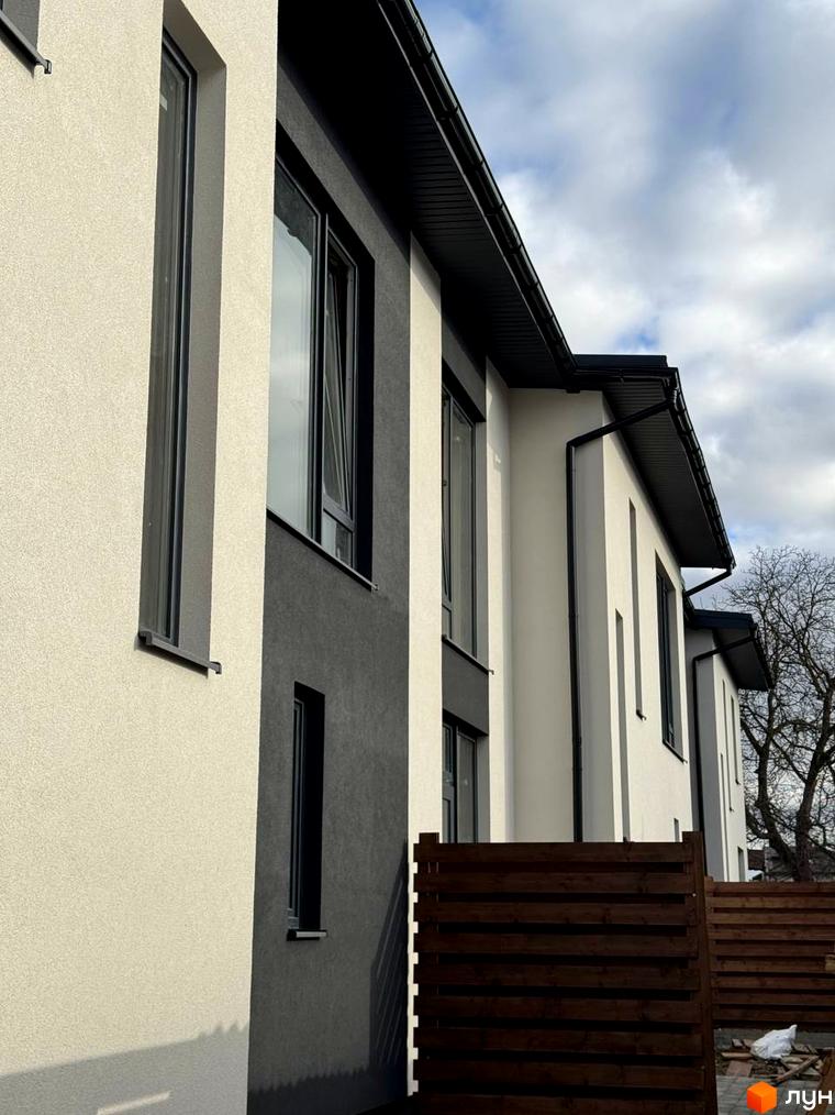 Котеджне містечко КМ Central Town. Фасад будинку з великими вікнами та темним дахом. На прибудинковій території дерев'яний паркан.