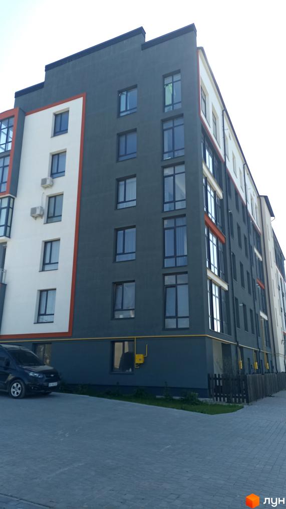 Фасад житлового комплексу на вул. Князя Володимира Великого, 8а, з сірими та білими елементами, вікнами та кондиціонерами. Поруч розташований паркінг з автомобілем та огорожа.