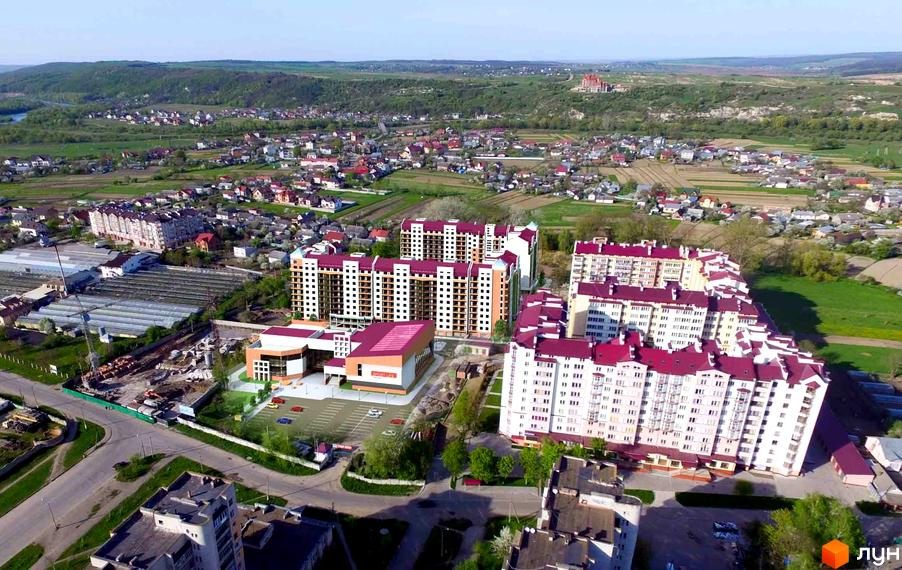 Зображення Житлового комплексу Затишна оселя з висоти пташиного польоту. На фото видно багатоповерхові будинки з червоними дахами та облаштовану прибудинкову територію.