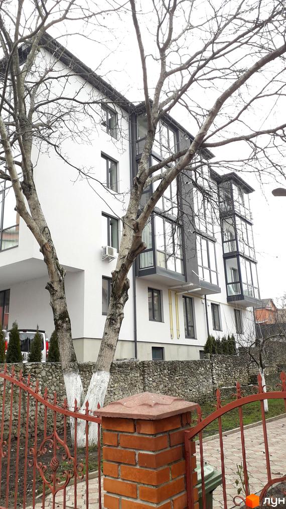 Зовнішній вигляд житлового комплексу на вул. Квітки Цісик, 54, з великими вікнами та балконами, оточений деревами та огороджений парканом.