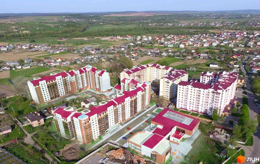 Зображення житлового комплексу Затишна оселя з висоти пташиного польоту. Багатоповерхові будинки з червоними дахами та облаштована прибудинкова територія.