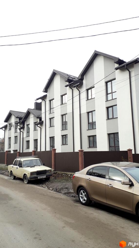 Новобудова на вулиці Квітки Цісик, 54а, б, в, г. Будинки з сірими та білими фасадами, з темними дахами та вікнами, розташовані вздовж вулиці з припаркованими автомобілями.