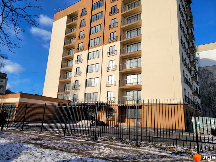 Житловий комплекс Темп - це багатоповерховий будинок з балконами та парканом навколо території. Фасад будівлі виконаний у світло-бежевих та коричневих тонах.