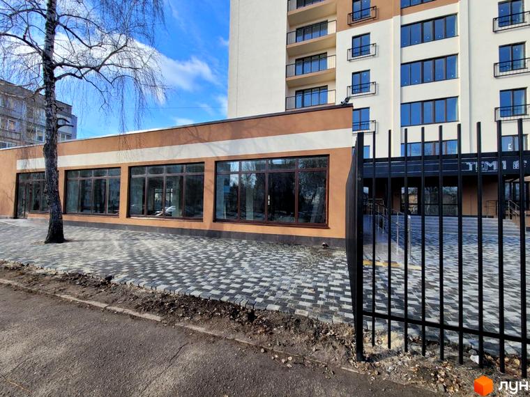 Житловий комплекс Темп з великими вікнами та огородженою територією. Поруч розташована доглянута прибудинкова територія з бруківкою та деревом.