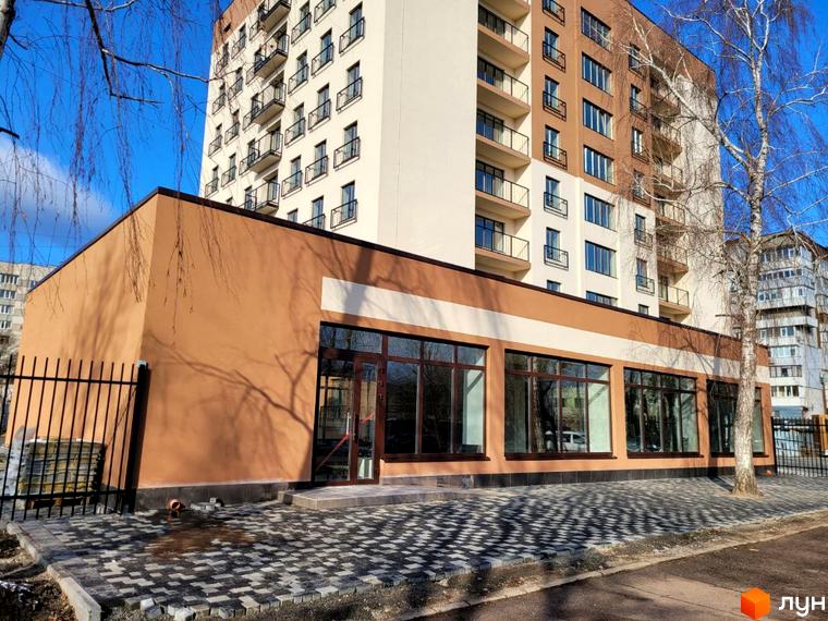 Зовнішній вигляд новобудови ЖК Темп з коричневим фасадом та великими вікнами, прибудинкова територія з бруківкою та огорожею.