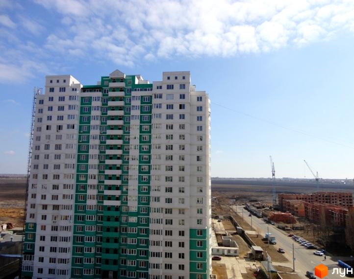 Житловий комплекс Європейський з фасадом у біло-зелених тонах. Прибудинкова територія з новими будівлями та доріжками.