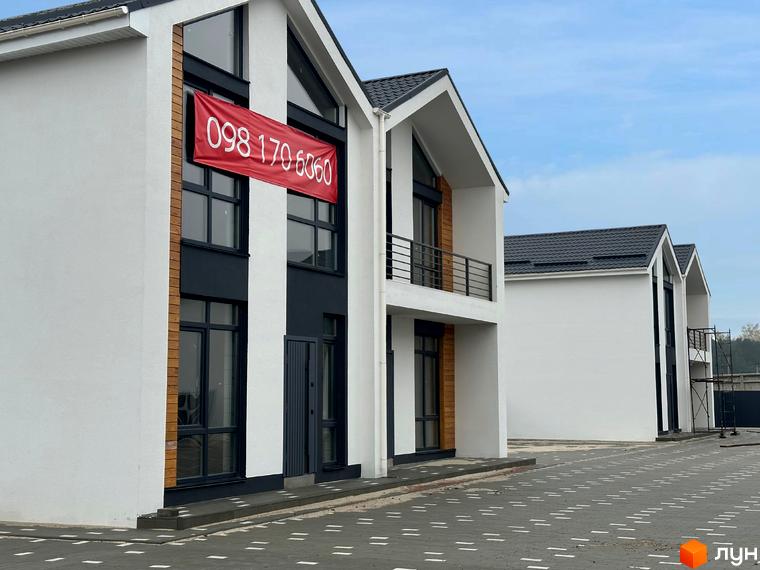 Сучасні дуплекси WoodSky з червоним банером з номером телефону на фасаді та вимощеною прибудинковою територією.