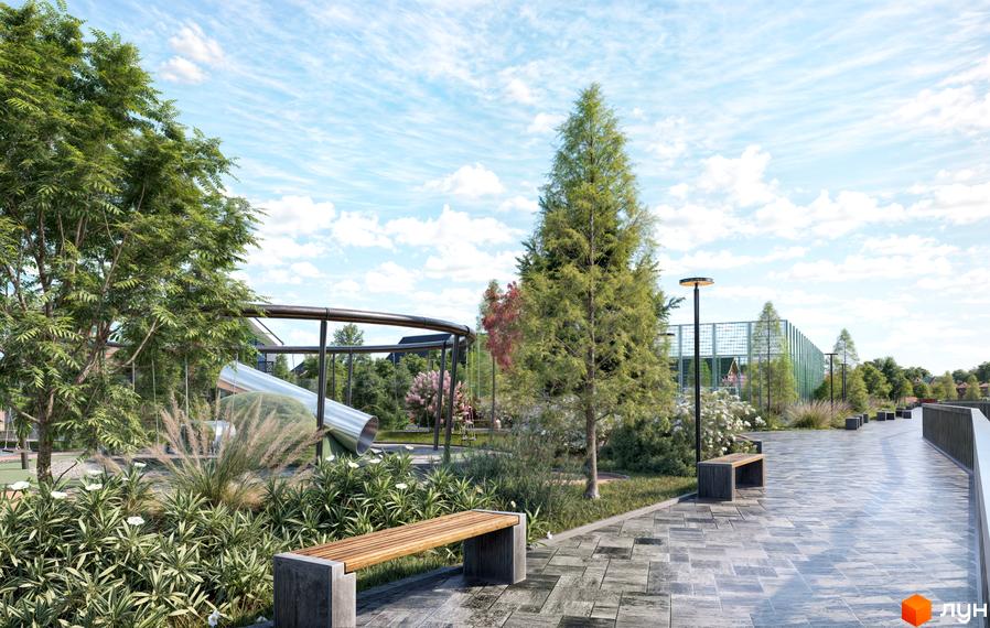 КМ Ovillas: дитячий майданчик з гіркою та лавками на бруківці біля зелених дерев та кущів під блакитним небом з хмарами.