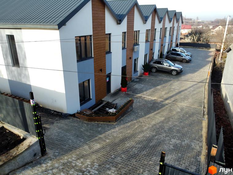 Таунхауси Klever House з сірим дахом та біло-блакитними фасадами, розташовані на бруківці з паркуванням.