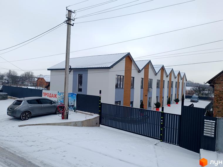 Таунхауси Klever House з біло-сірими фасадами та дерев'яними вставками, розташовані на засніженій території з парканом та парковкою.