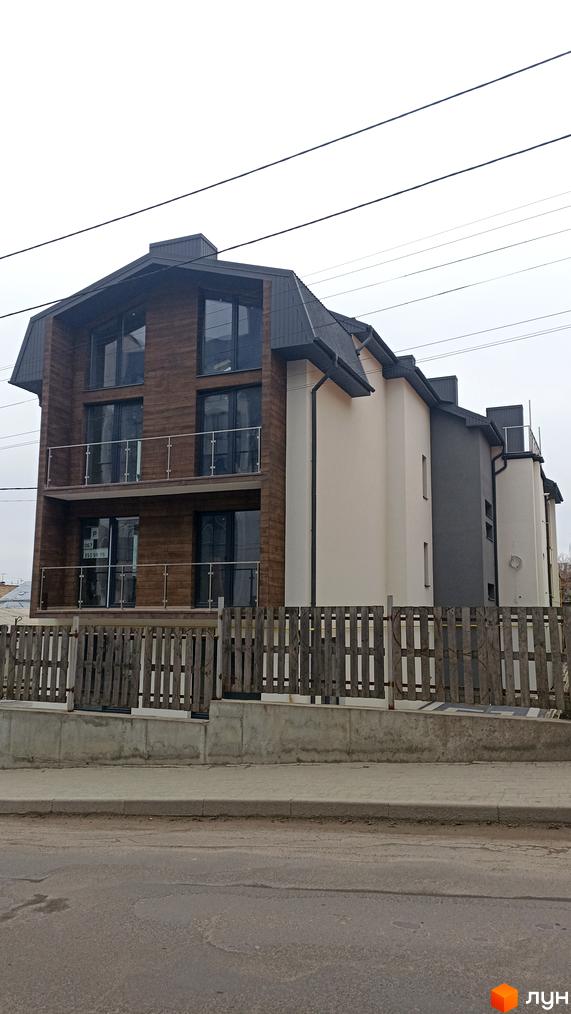 Фасад новобудови на вул. Весела, 46, з дерев'яним оздобленням та скляними балконами, огороджений дерев'яним парканом.