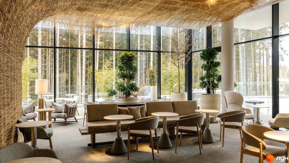 Інтер'єр апарт-комплексу Mountain Residence з панорамними вікнами та видом на ліс. Затишна зона відпочинку з диванами та кріслами біля каміна.