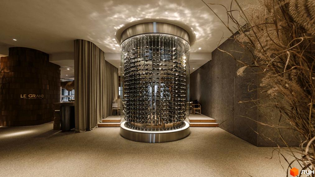 Апарт-комплекс Mountain Residence з вражаючою циліндричною винною шафою в центрі просторого залу. Інтер'єр оформлений у природних тонах з акцентом на дерево та текстиль.