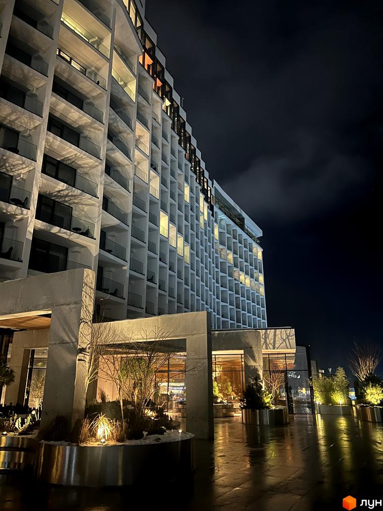 Апарт-комплекс Mountain Residence у вечірній час з підсвіченими вікнами та балконами, що виходять на доглянуту прибудинкову територію з освітленими рослинами.