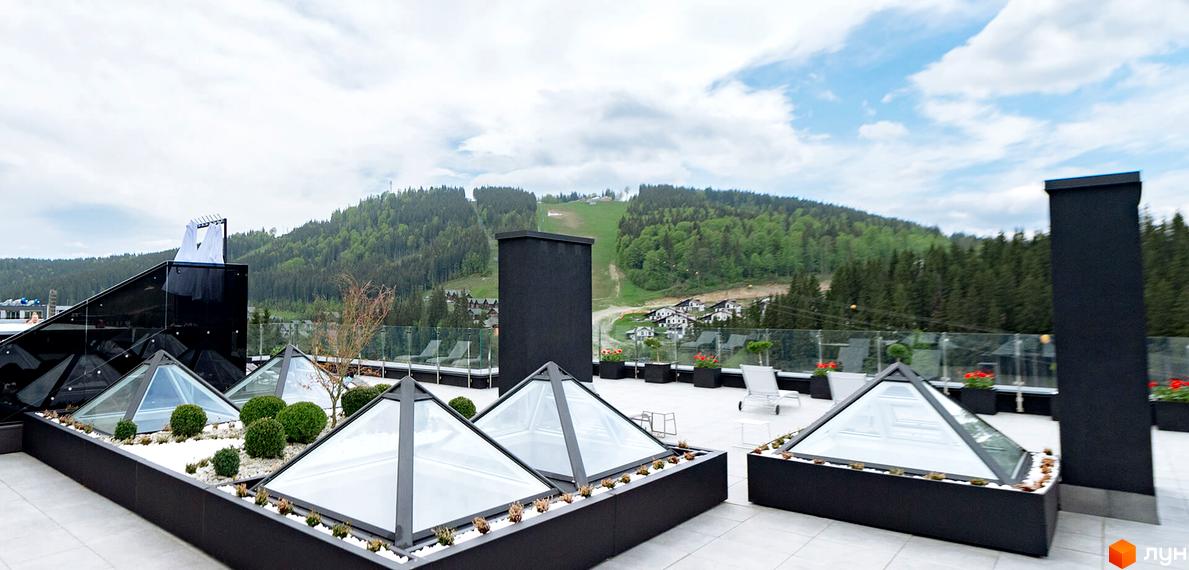 BUKA Apart-Hotel: тераса з пірамідальними скляними дахами та панорамним видом на гори. Навколо зелені насадження та зони відпочинку.