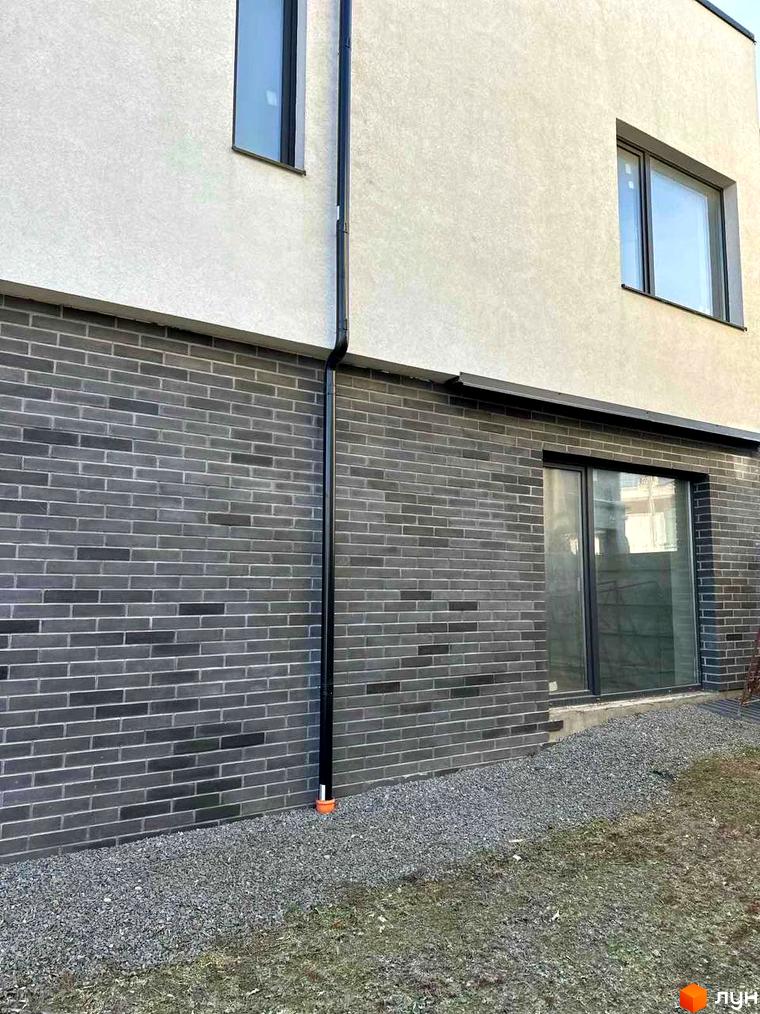 Фасад житлового комплексу на вул. Пилипа Орлика, 51, з сірою цегляною кладкою та великими вікнами. Поруч гравійна доріжка та зелена ділянка.