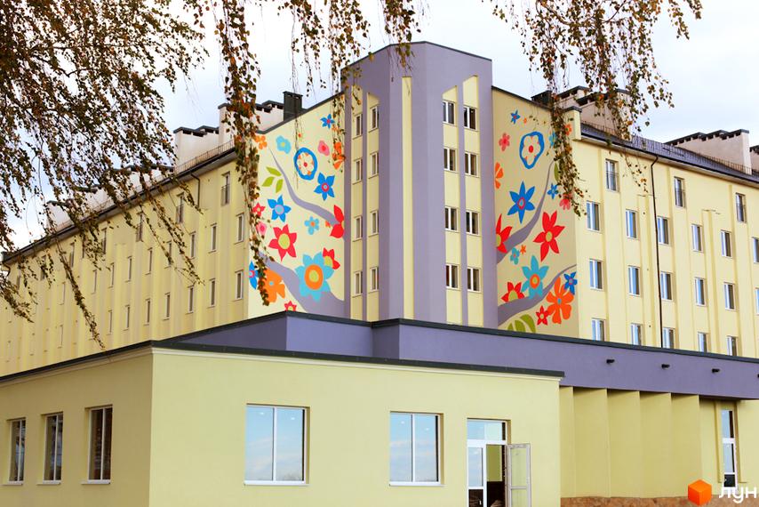 Зображення фасаду Житлового комплексу Сонячний з яскравим розписом. Світла будівля з великими вікнами та прилеглою територією.