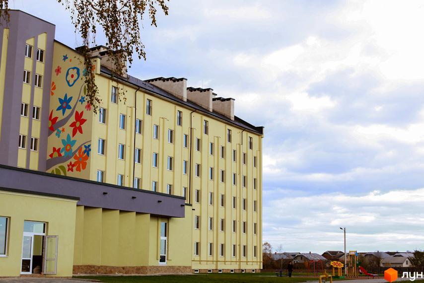 Зображення фасаду Житлового комплексу Сонячний з яскравим розписом. На передньому плані дитячий майданчик та зелена територія.