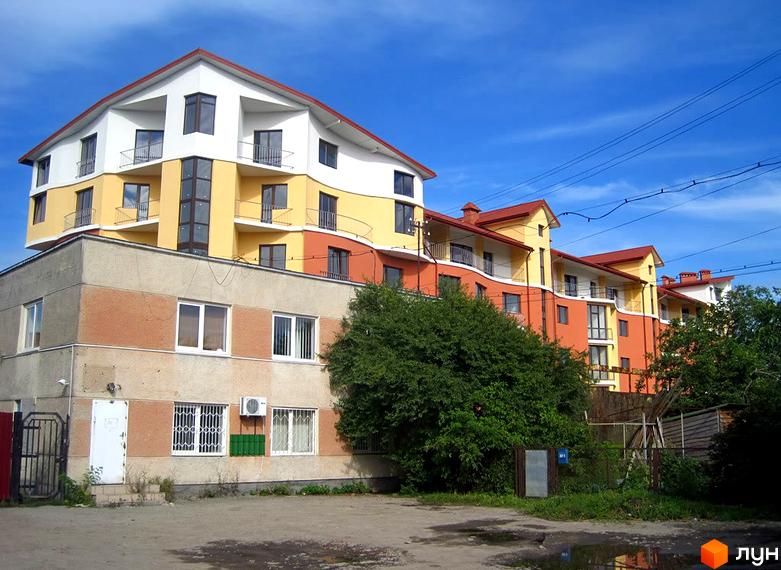 Зображення фасаду та прибудинкової території Новобудови Перлина. Багатоповерховий будинок з балконами, поруч зелені насадження та невелика парковка.